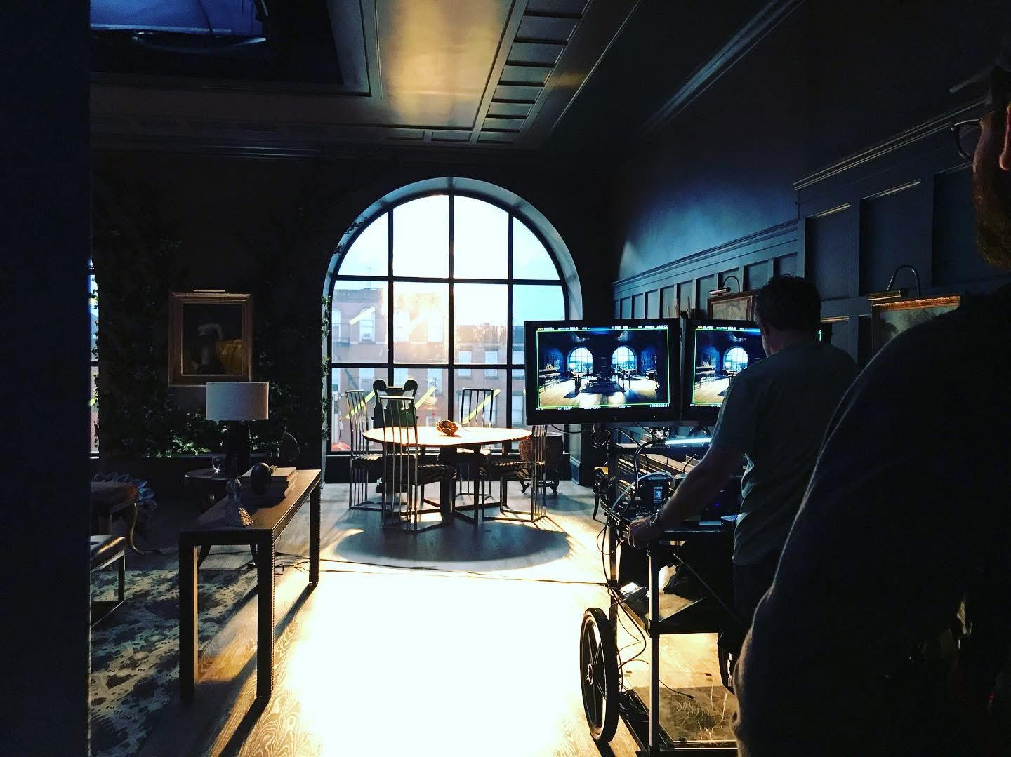 A real production set with strong daylight through an arched window and camera monitors